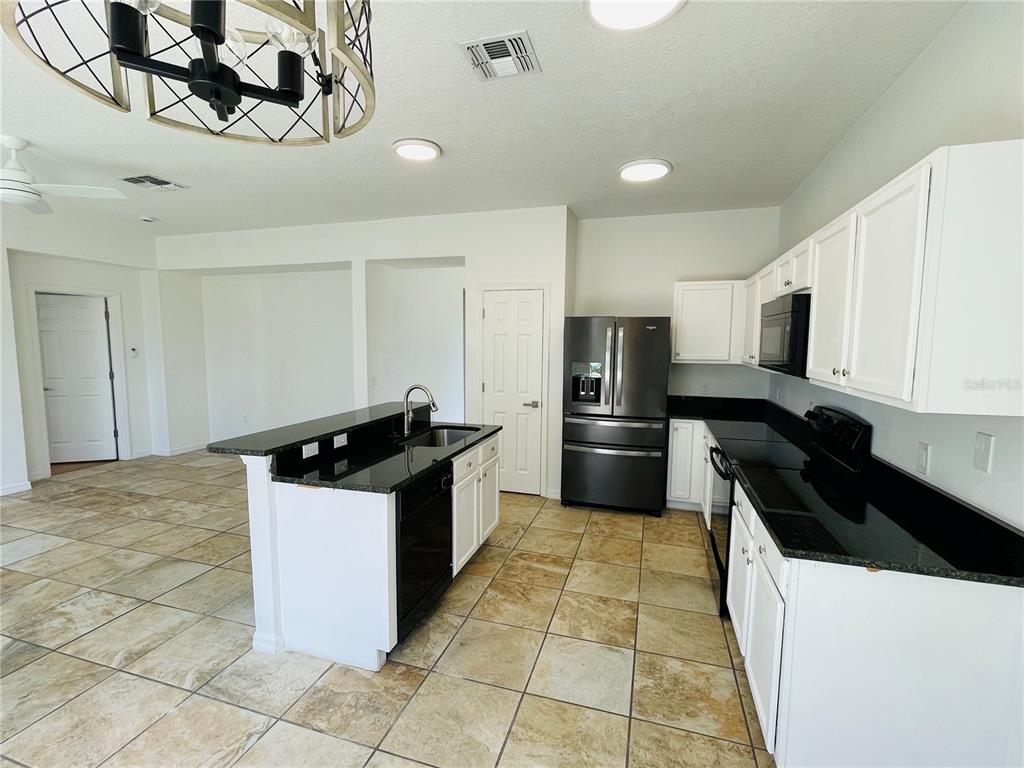 A kitchen features white cabinets, black countertops, stainless steel appliances, and tiled flooring — 2728 PORTCHESTER COURT, KISSIMMEE, FL