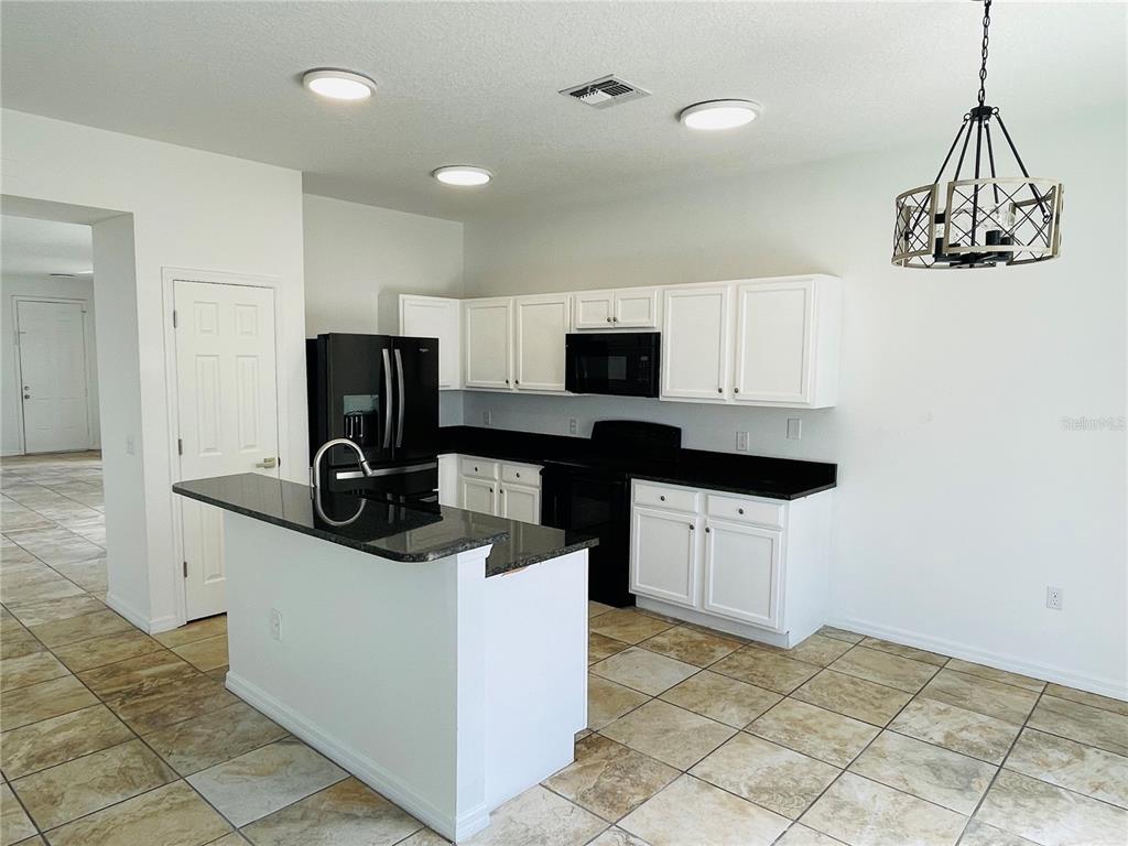 A kitchen features white cabinets, black countertops, black appliances, and tan tile flooring — 2728 PORTCHESTER COURT, KISSIMMEE, FL