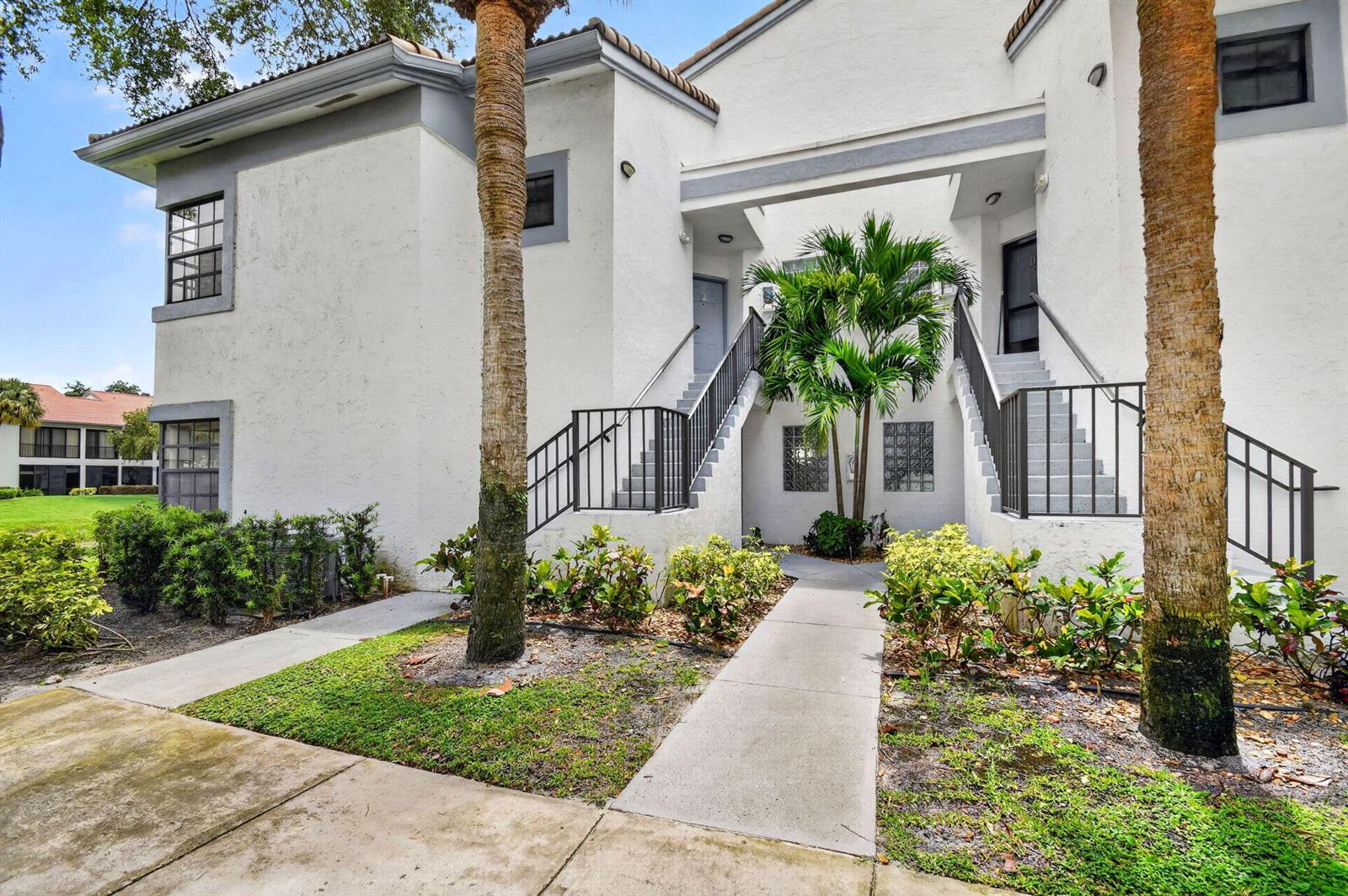 A two-story white stucco apartment building features exterior staircases and a central palm tree — 5395 Firenze Drive # B, Boynton Beach FL 33437, BOYNTON BEACH, FL