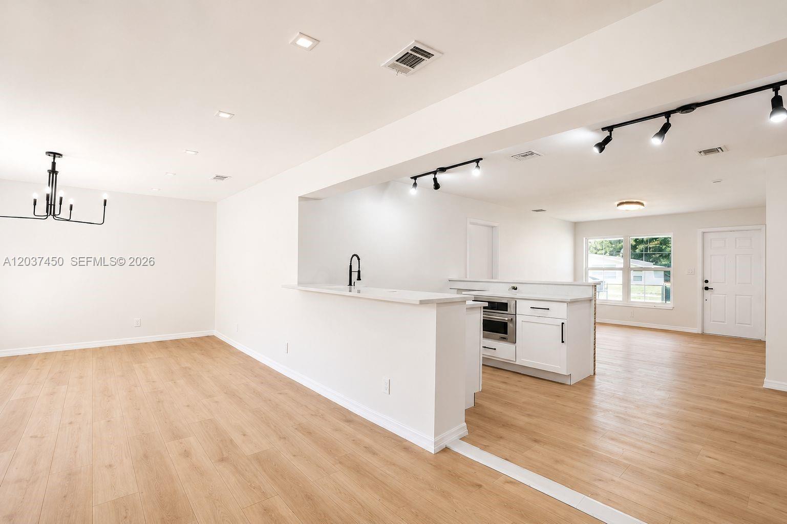 An open-concept kitchen and dining area features white cabinetry, light wood flooring, and track lighting — 3460 NW 17th St, Lauderhill FL 33311, LAUDERHILL, FL