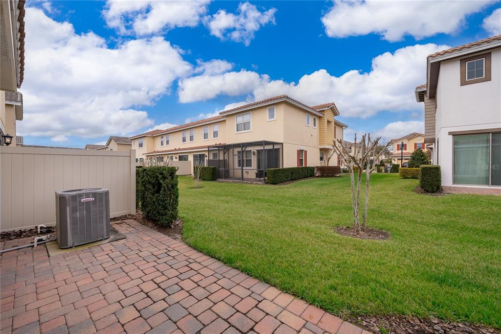 A paved patio with an air conditioning unit overlooks a grassy backyard and townhouses — 14044 MILLINGTON STREET, ORLANDO, FL