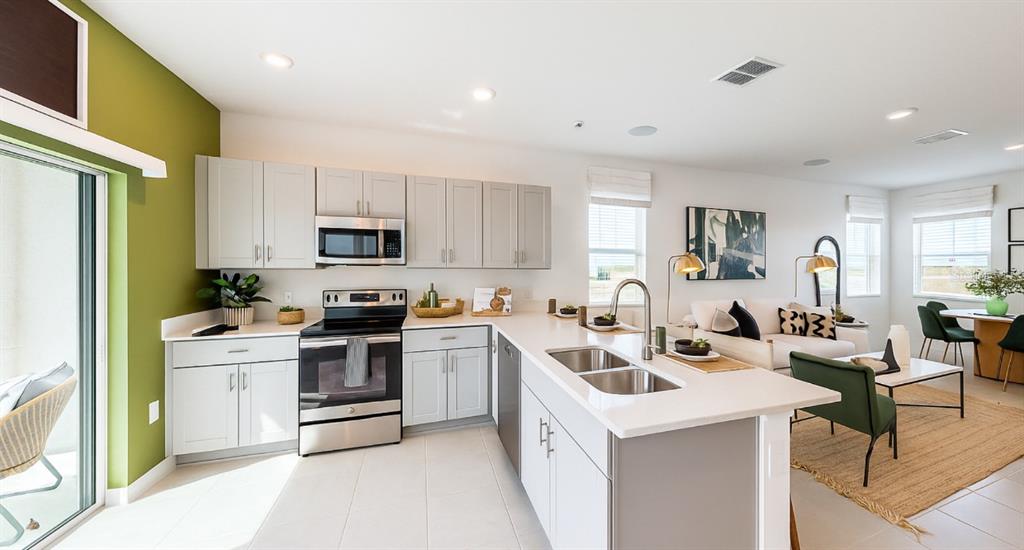 A modern kitchen with light gray cabinets, stainless steel appliances, and an island with seating — 2004 VIEWFINDER STREET, KISSIMMEE, FL