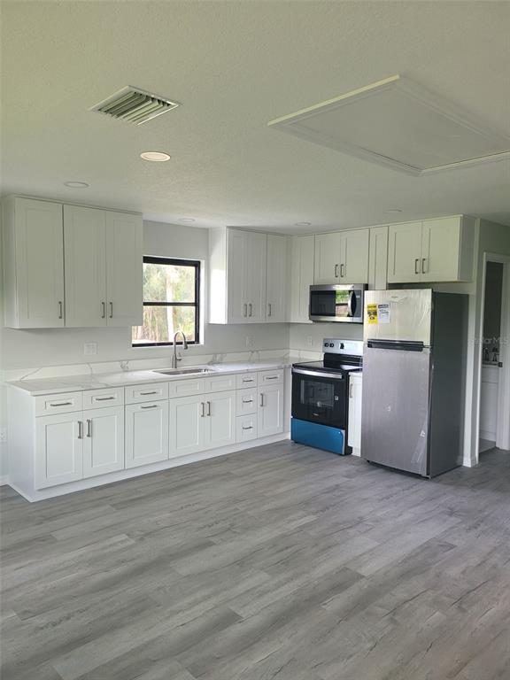 A kitchen features white cabinets, stainless steel appliances, marble-look countertops, and gray wood-look flooring — 2331 MISSION VALLEY BOULEVARD, NOKOMIS, FL