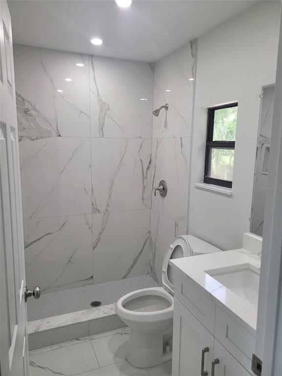 A small bathroom features a walk-in shower with white marble-look tile, a toilet, and vanity — 2331 MISSION VALLEY BOULEVARD, NOKOMIS, FL