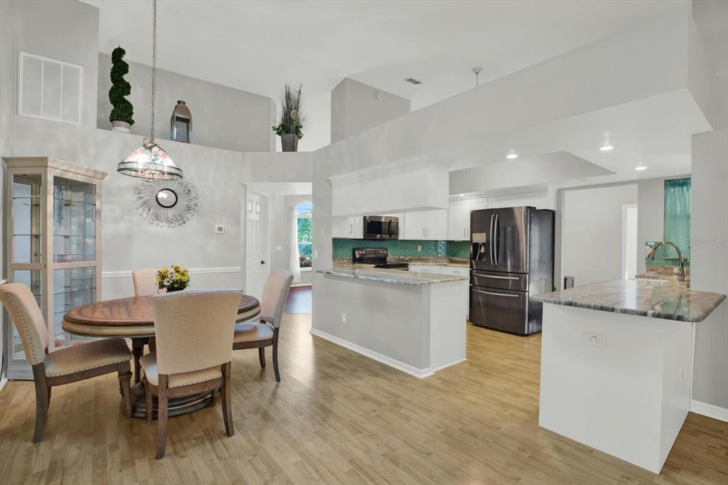 A dining area with a table and chairs opens into a kitchen with white cabinets — 5924 WILLOW CREEK COURT, NEW PORT RICHEY, FL