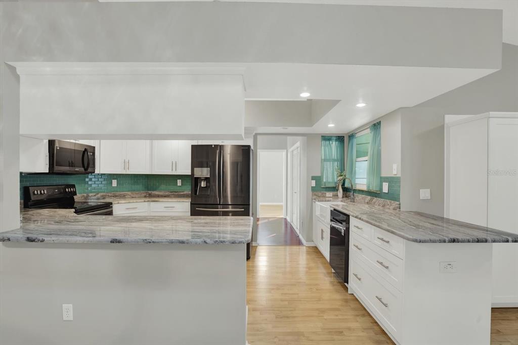 A kitchen features white cabinets, marble-patterned countertops, a green tile backsplash, and stainless steel appliances — 5924 WILLOW CREEK COURT, NEW PORT RICHEY, FL