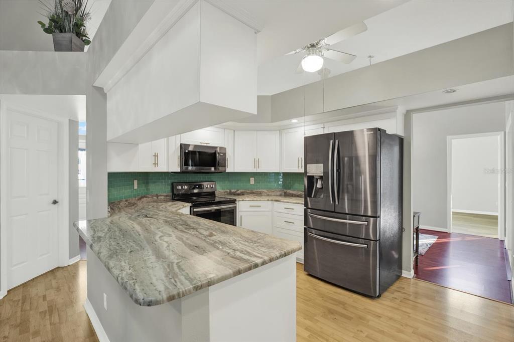 A kitchen features white cabinets, a green tile backsplash, granite countertops, and stainless steel appliances — 5924 WILLOW CREEK COURT, NEW PORT RICHEY, FL
