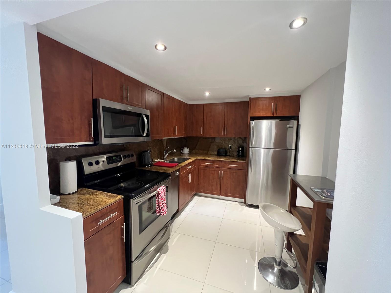 A kitchen features wood cabinets, stainless steel appliances, granite countertops, and white tile flooring — 5161 Collins Ave # 309, Miami Beach FL 33140, MIAMI BEACH, FL