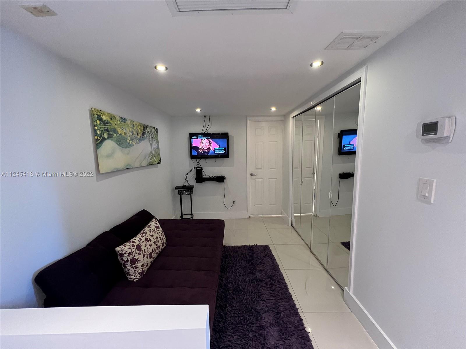 A small room features a purple sofa, a wall-mounted television, and mirrored closet doors — 5161 Collins Ave # 309, Miami Beach FL 33140, MIAMI BEACH, FL