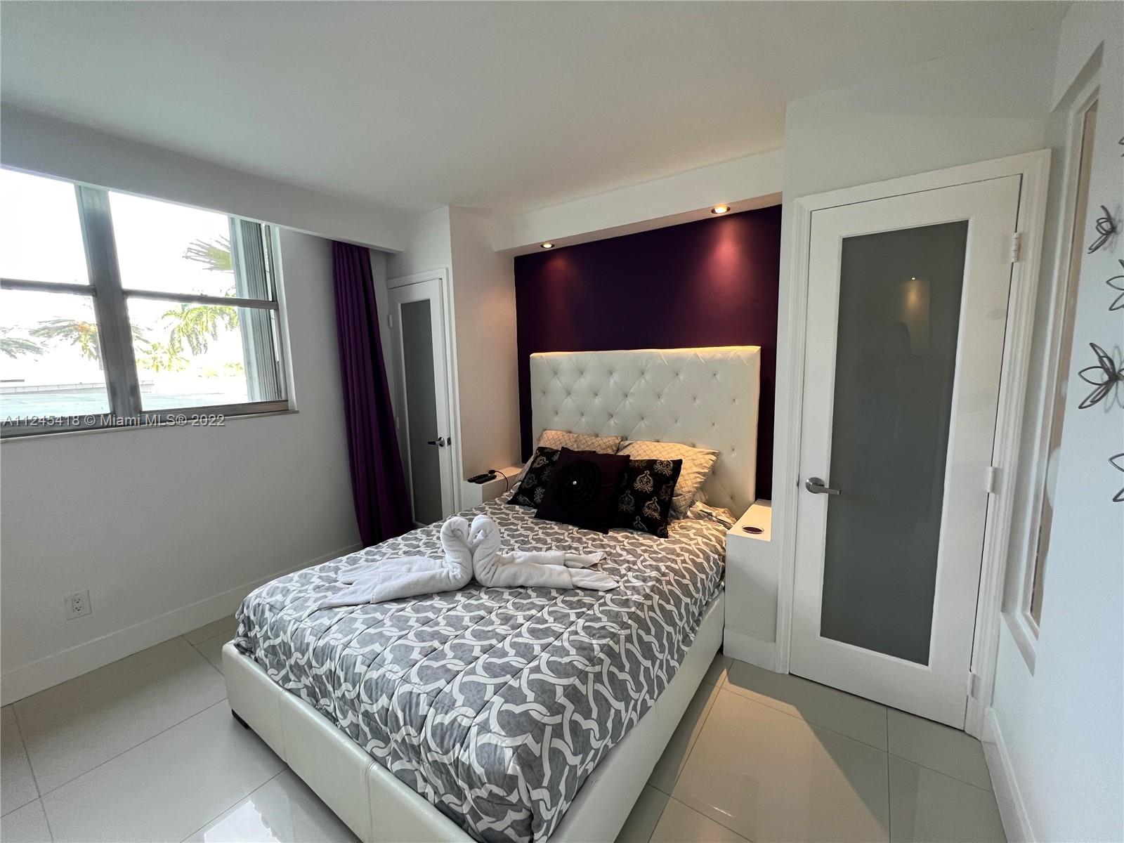 A bedroom features a white tufted headboard against a purple wall with recessed lighting — 5161 Collins Ave # 309, Miami Beach FL 33140, MIAMI BEACH, FL