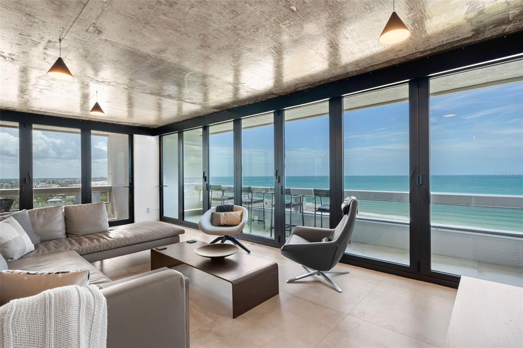 A modern living room features a concrete ceiling, floor-to-ceiling windows, and a balcony overlooking ocean — 5400 OCEAN BOULEVARD UNIT #15 1-4, SARASOTA, FL