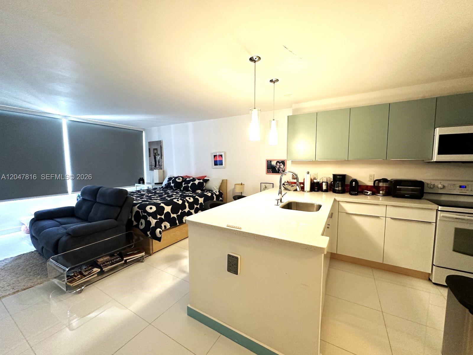 A studio apartment features a kitchen with light green cabinets, a white island, and a bed — 1000 West Ave # 1532, Miami Beach FL 33139, MIAMI BEACH, FL