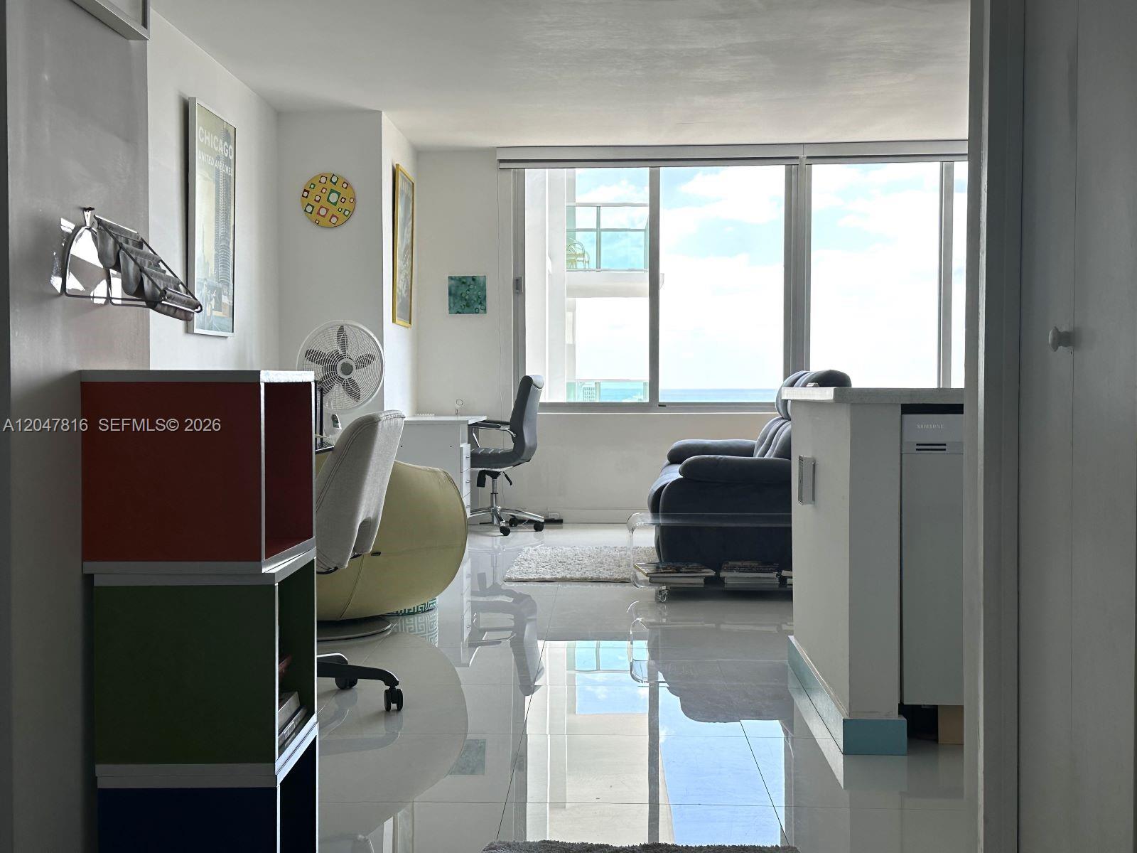 A bright living area with white tile floors, a desk, and ocean views through windows — 1000 West Ave # 1532, Miami Beach FL 33139, MIAMI BEACH, FL
