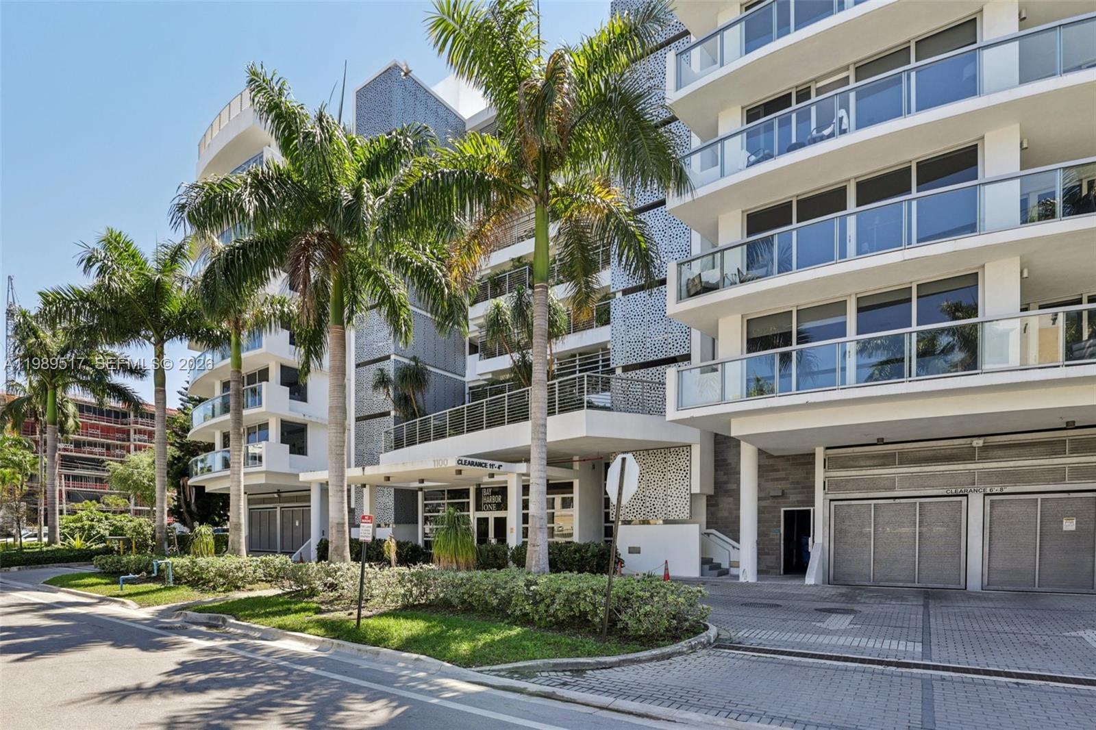 A low-angle exterior view of a modern multi-story apartment building with palm trees — 1100 100th St # 703, Bay Harbor Islands FL 33154, BAY HARBOR ISLANDS, FL