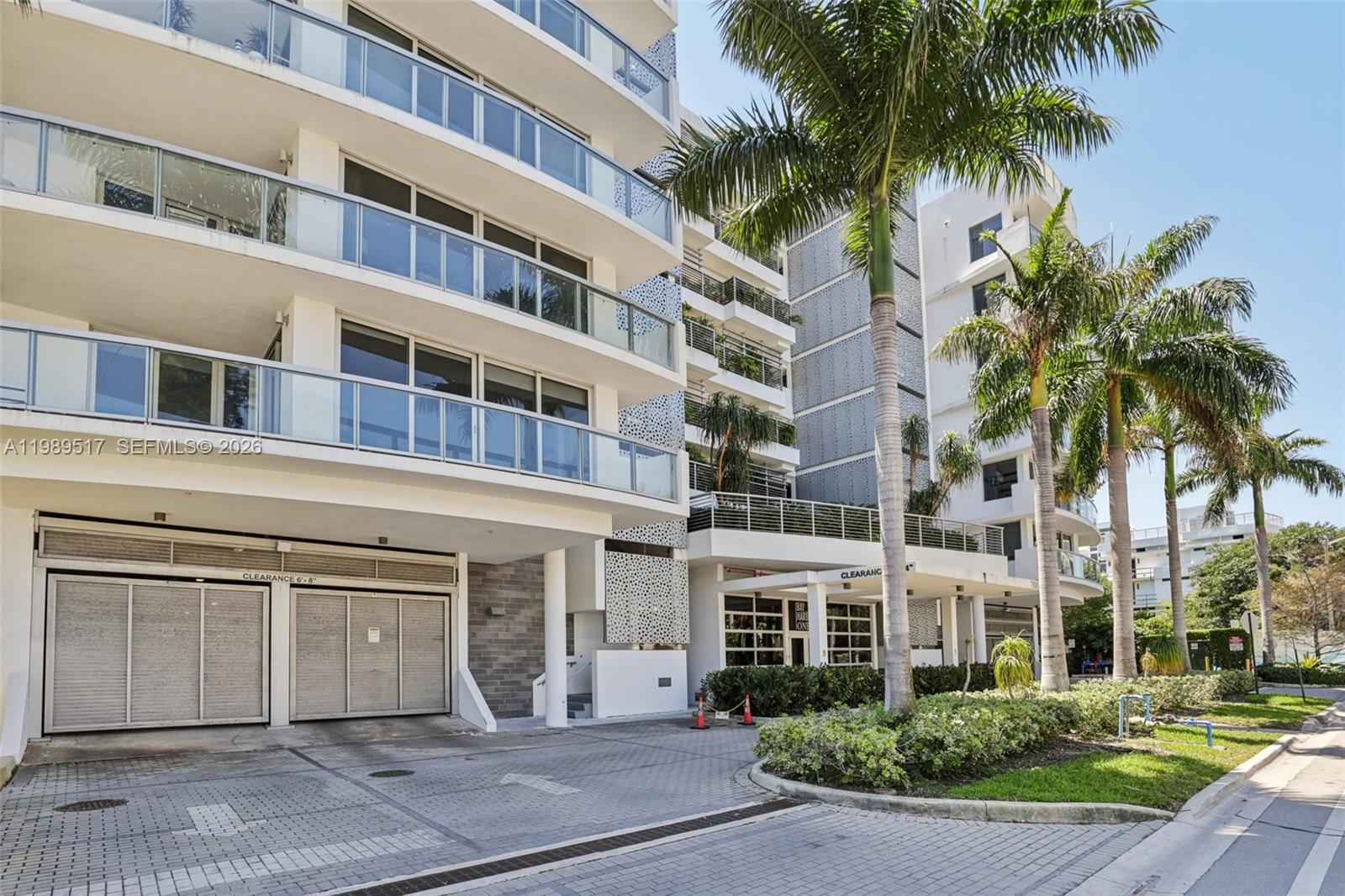 The exterior of a modern multi-story apartment building features glass balconies and a parking garage — 1100 100th St # 703, Bay Harbor Islands FL 33154, BAY HARBOR ISLANDS, FL