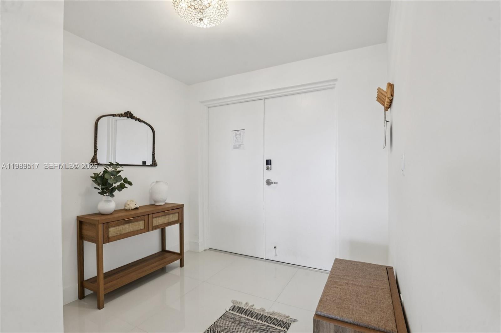 A bright entryway features white walls, tile flooring, a wooden console table, and double doors — 1100 100th St # 703, Bay Harbor Islands FL 33154, BAY HARBOR ISLANDS, FL