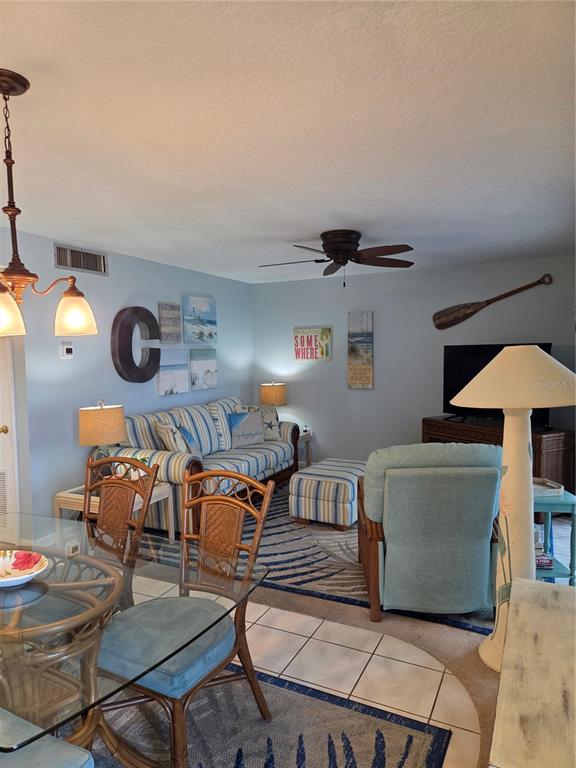 A living room with a striped sofa, a blue armchair, and a glass dining table — 3150 N ATLANTIC AVENUE UNIT 4-770, COCOA BEACH, FL