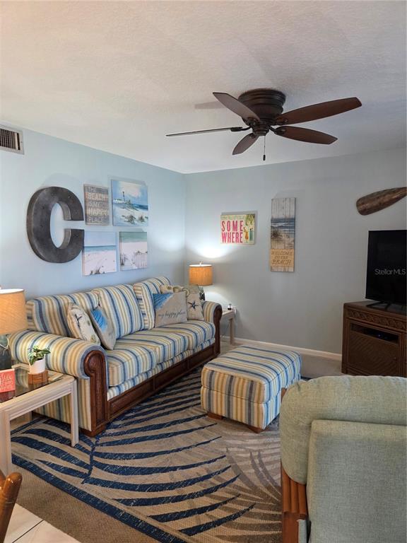 A living room features a striped sofa, matching ottoman, coastal decor, and a ceiling fan — 3150 N ATLANTIC AVENUE UNIT 4-770, COCOA BEACH, FL