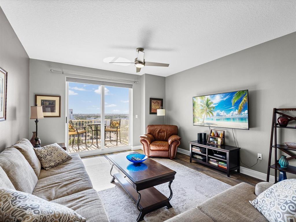 A living room features a sofa, leather armchair, coffee table, television, and a balcony view — 628 CLEVELAND STREET UNIT 1011, CLEARWATER, FL