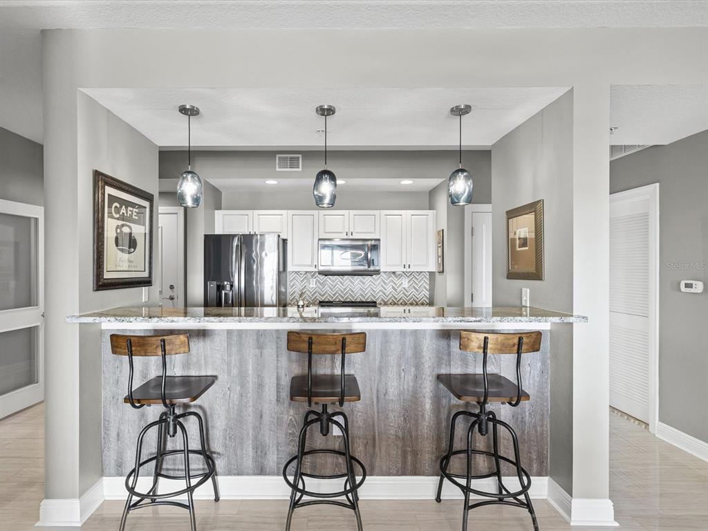 A kitchen features a breakfast bar with three stools, white cabinets, and a herringbone backsplash — 628 CLEVELAND STREET UNIT 1011, CLEARWATER, FL
