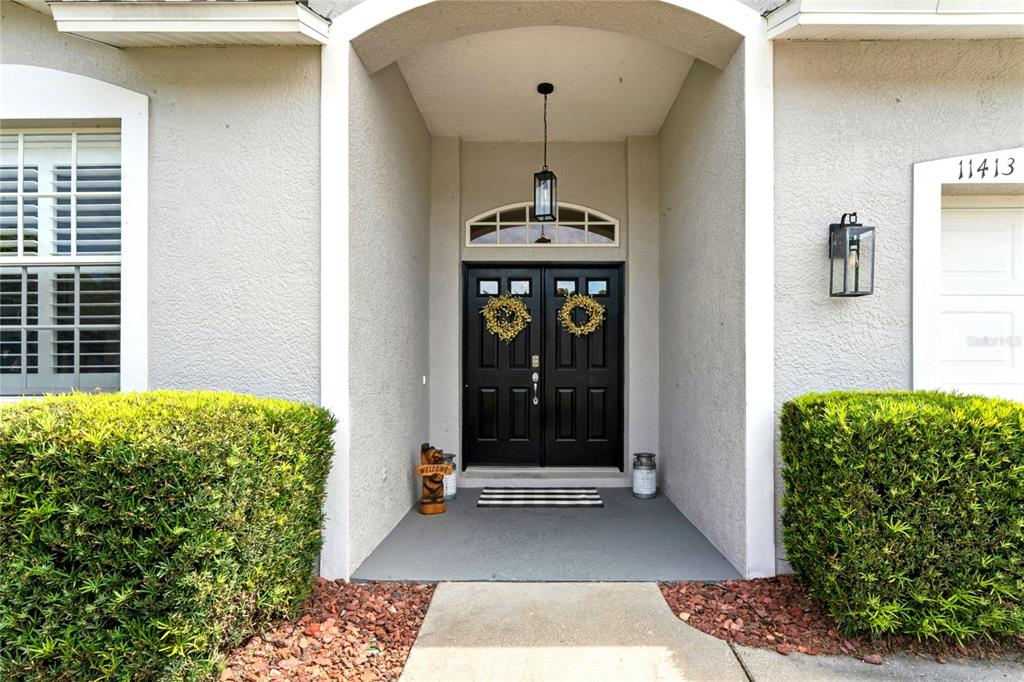 A front entryway features black double doors with wreaths under a covered porch — 11413 BLOOMINGTON COURT, NEW PORT RICHEY, FL