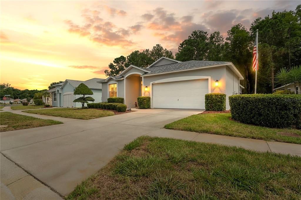 A single-story suburban house with a two-car garage and a manicured lawn at sunset — 11413 BLOOMINGTON COURT, NEW PORT RICHEY, FL