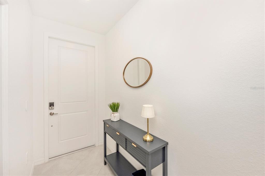A white-walled entryway features a dark console table, a small lamp, and a round mirror — 17625 OPAL SAND DRIVE UNIT 207, VENICE, FL