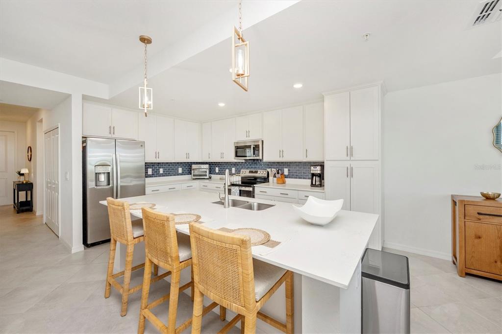 A modern kitchen features white cabinetry, a large quartz island, and a blue tile backsplash — 17625 OPAL SAND DRIVE UNIT 207, VENICE, FL