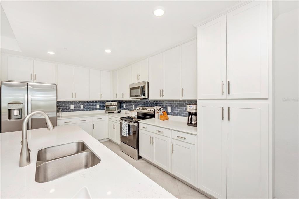 A modern kitchen features white cabinetry, stainless steel appliances, a quartz island, and blue backsplash — 17625 OPAL SAND DRIVE UNIT 207, VENICE, FL