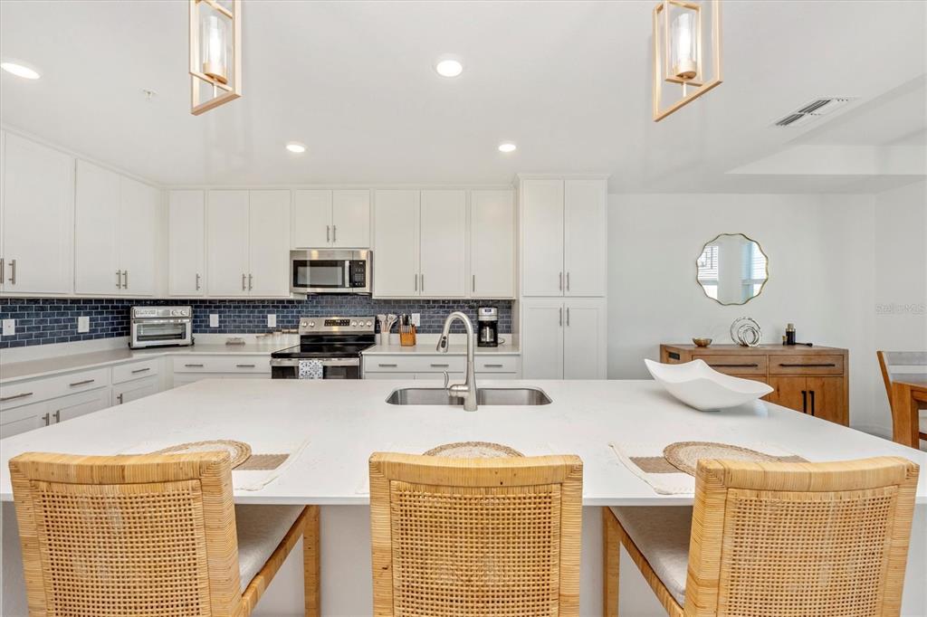 A kitchen features white cabinetry, a large island with bar seating, and a blue backsplash — 17625 OPAL SAND DRIVE UNIT 207, VENICE, FL