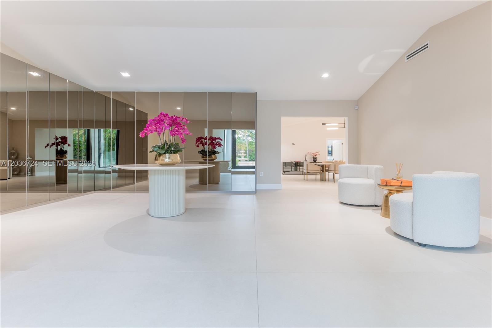 A bright, minimalist foyer features a mirrored wall, a central pedestal table, and two white chairs — 7300 SW 77th Ave, Miami FL 33143, MIAMI, FL
