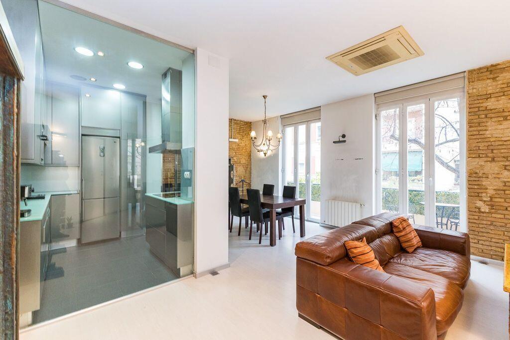 A modern kitchen behind a glass wall overlooks a living area with a leather sofa — 26 Carrer Del Mestre Gozalbo, FL