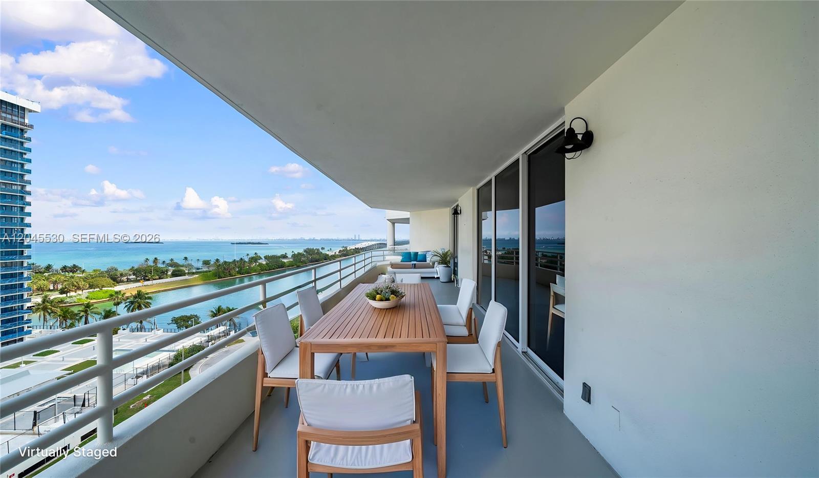 A balcony with a wooden dining set overlooks a body of water and city skyline — 555 NE 34th St # 2704, Miami FL 33137, MIAMI, FL