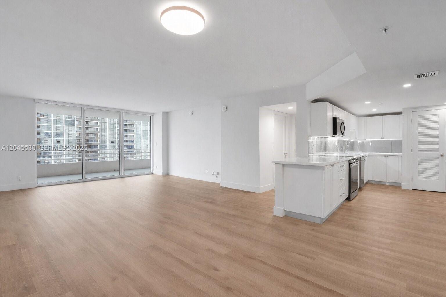 An open-concept living area features light wood floors, white cabinetry, and floor-to-ceiling glass doors — 555 NE 34th St # 2704, Miami FL 33137, MIAMI, FL