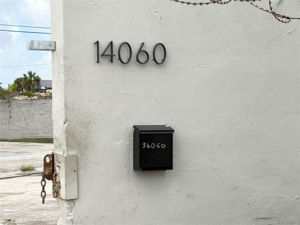 A white concrete wall displays the house number 14060 above a black mailbox — 14060 NW 19TH AVENUE, OPA LOCKA, FL
