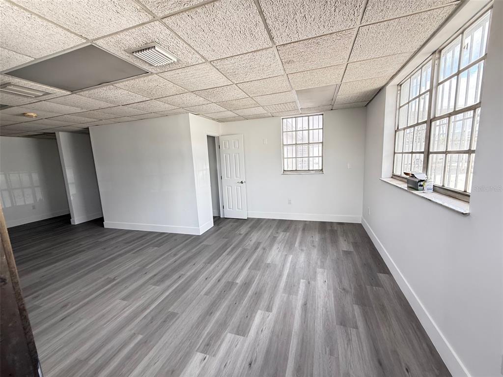 An empty office space features gray wood-look flooring, white walls, and a drop ceiling — 14060 NW 19TH AVENUE, OPA LOCKA, FL