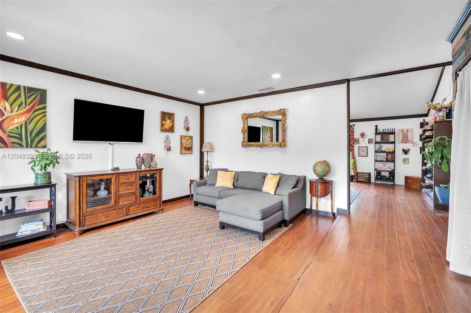 A living room features a grey sectional sofa, wooden media console, and hardwood floors — 2401 NW 110th Ter # 2401, Sunrise FL 33322, SUNRISE, FL