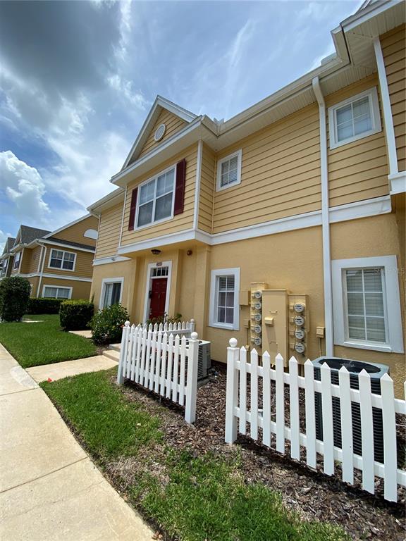 A yellow two-story townhouse exterior with a white picket fence and utility meters — 4552 JONAFREE LANE UNIT 101, KISSIMMEE, FL