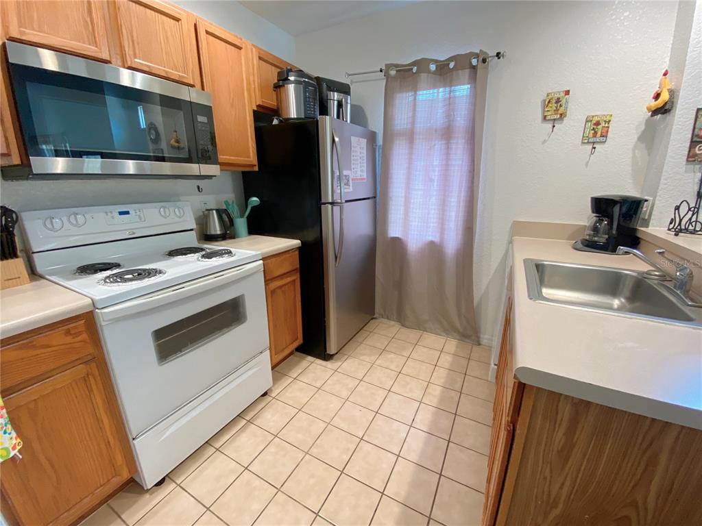 A kitchen features wood cabinets, a white stove, a stainless steel refrigerator, and tiled flooring — 4552 JONAFREE LANE UNIT 101, KISSIMMEE, FL