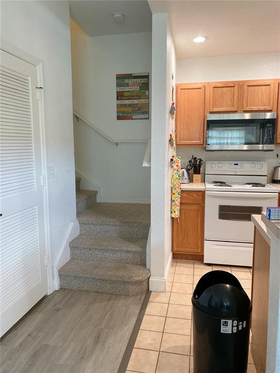 A kitchen with light wood cabinets and white appliances sits next to carpeted stairs — 4552 JONAFREE LANE UNIT 101, KISSIMMEE, FL