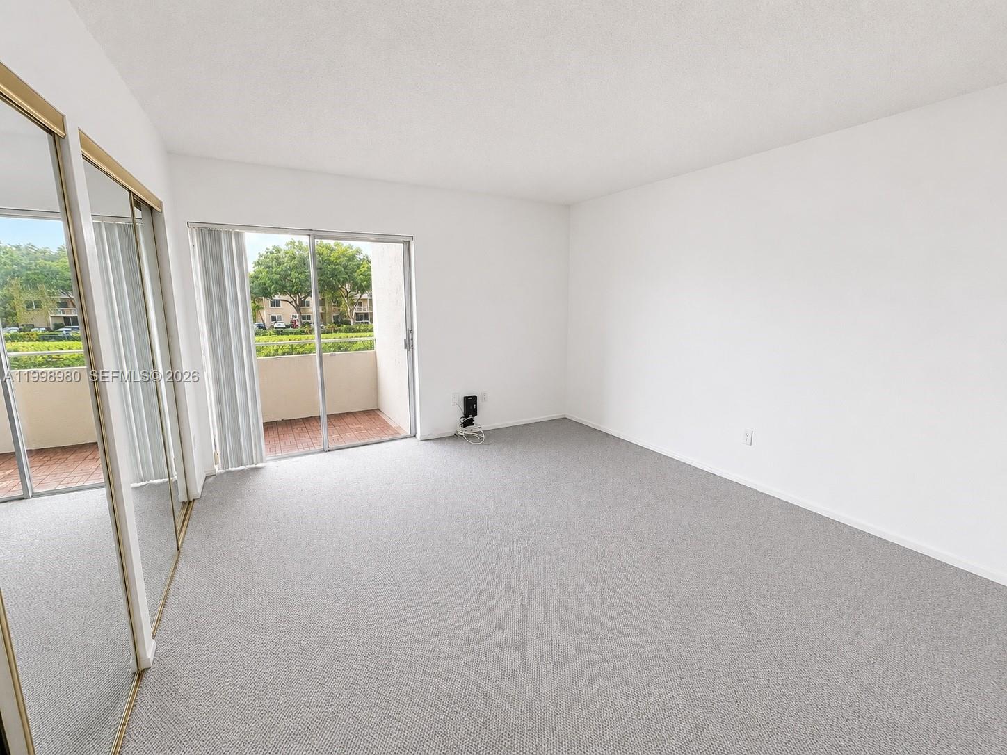 An empty bedroom features gray carpeting, white walls, mirrored closet doors, and a sliding glass door — 7787 SW 86th St # 206, Miami FL 33143, MIAMI, FL