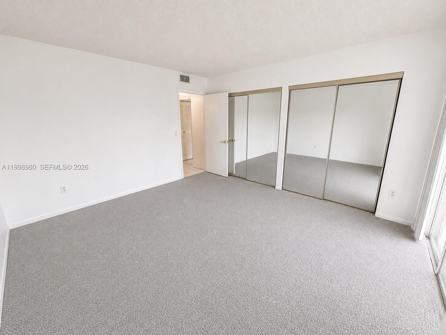 A bedroom features gray carpeting, white walls, and two sets of mirrored sliding closet doors — 7787 SW 86th St # 206, Miami FL 33143, MIAMI, FL
