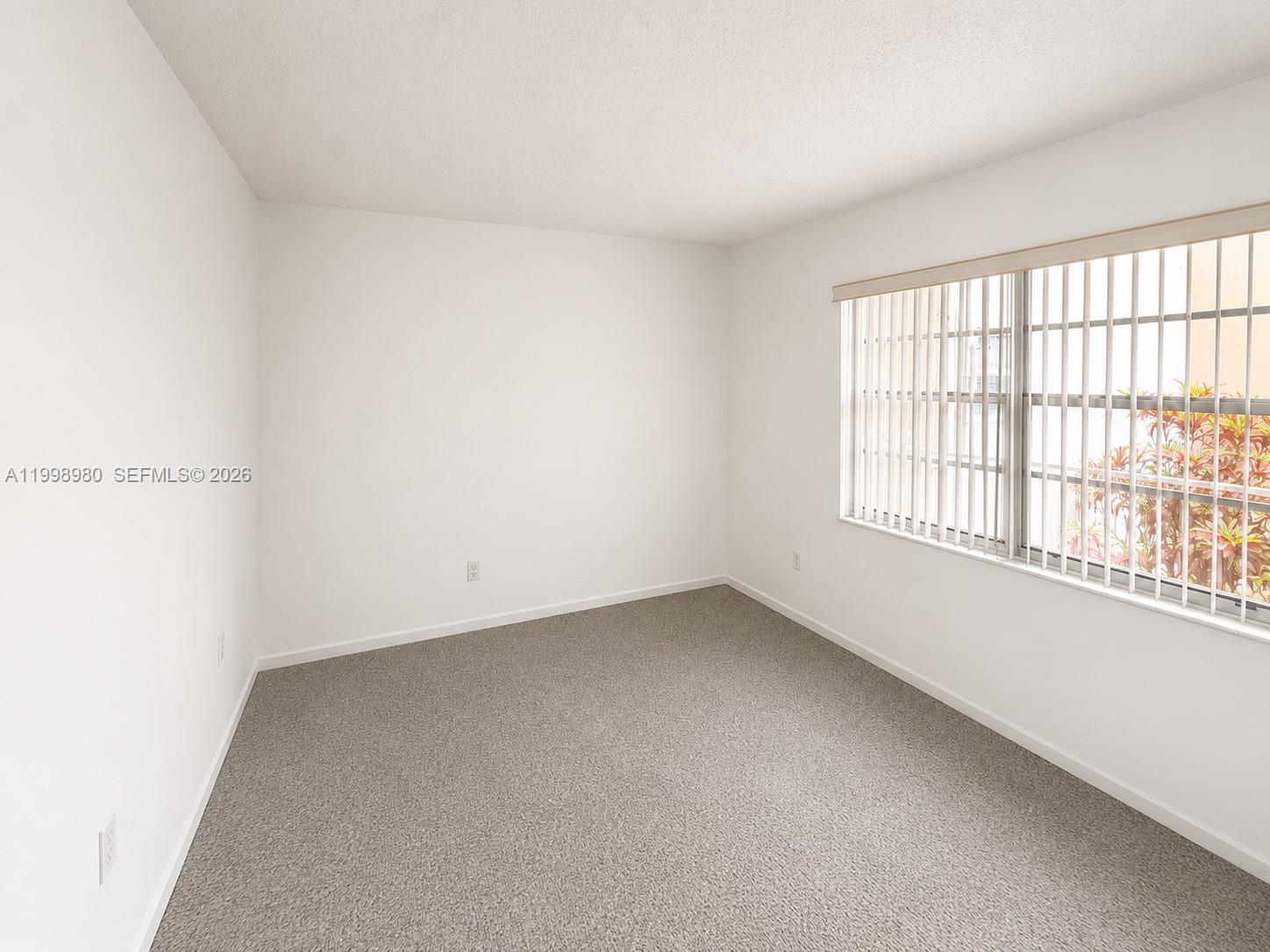 An empty bedroom features white walls, beige carpeting, and a window with vertical blinds — 7787 SW 86th St # 206, Miami FL 33143, MIAMI, FL