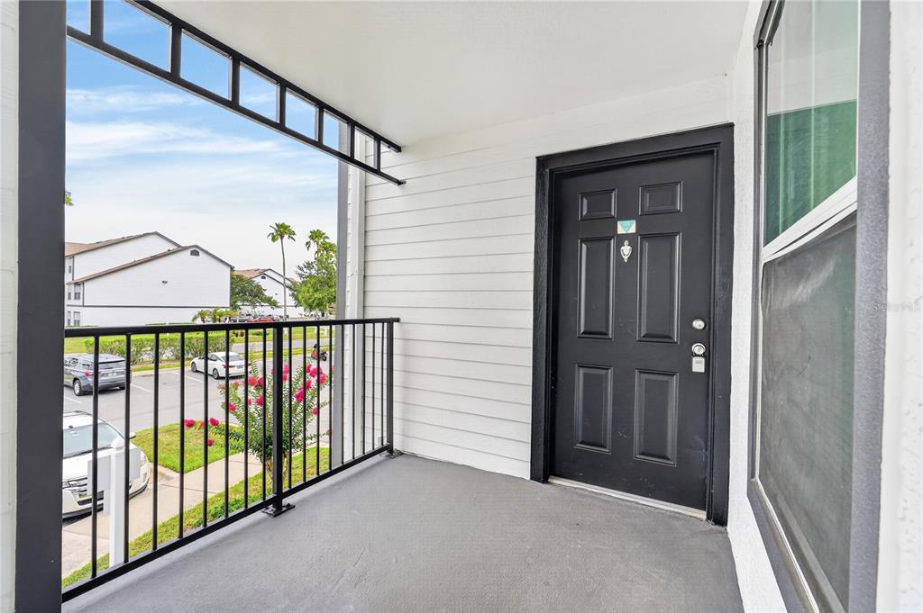A covered apartment balcony features a black door, gray flooring, and a black metal railing — 4103 TROPICAL ISLE BLVD UNIT 123, KISSIMMEE, FL
