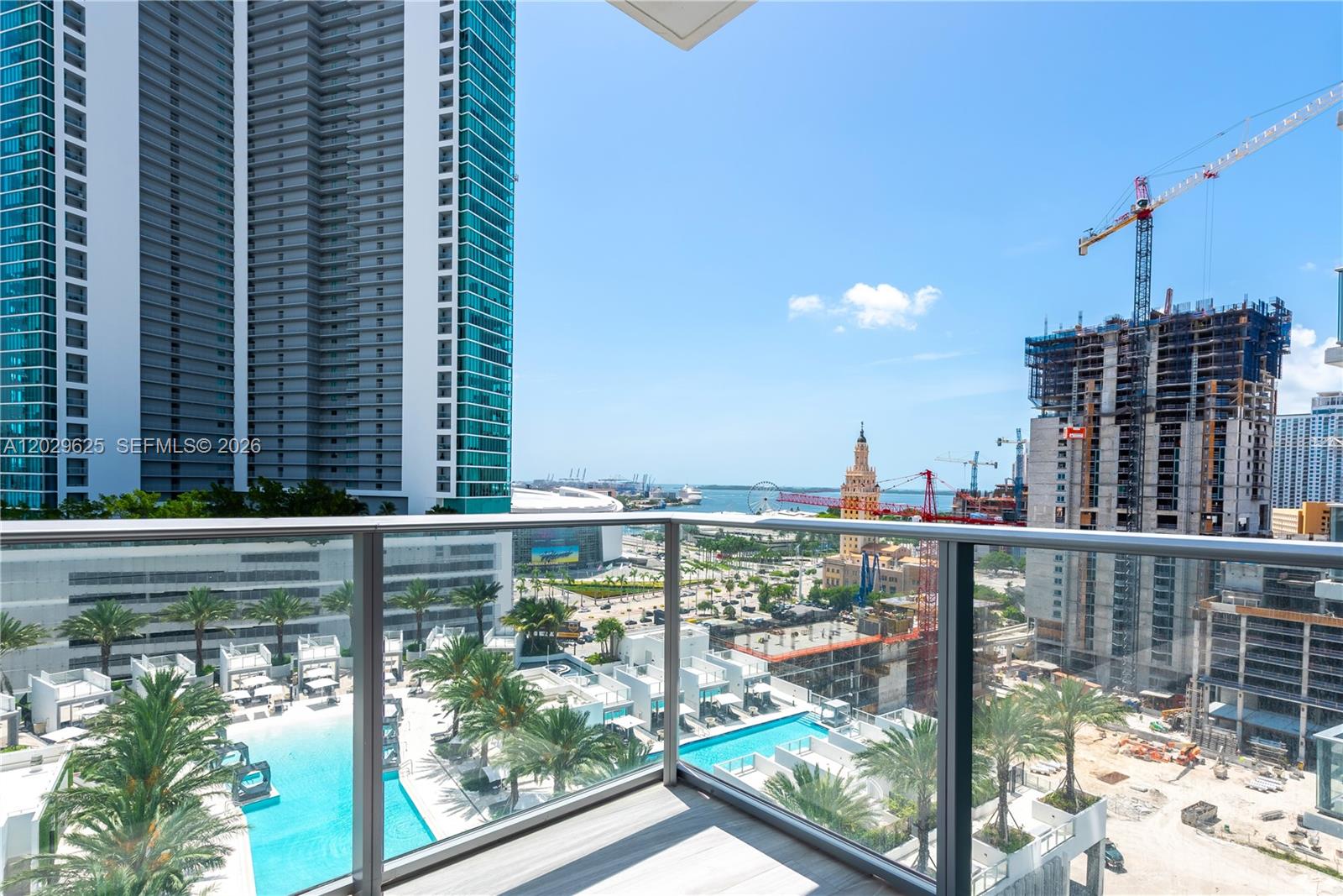 A high-rise balcony overlooks a swimming pool, urban construction, and a distant harbor — 851 NE 1st Ave # 1705, Miami FL 33132, MIAMI, FL
