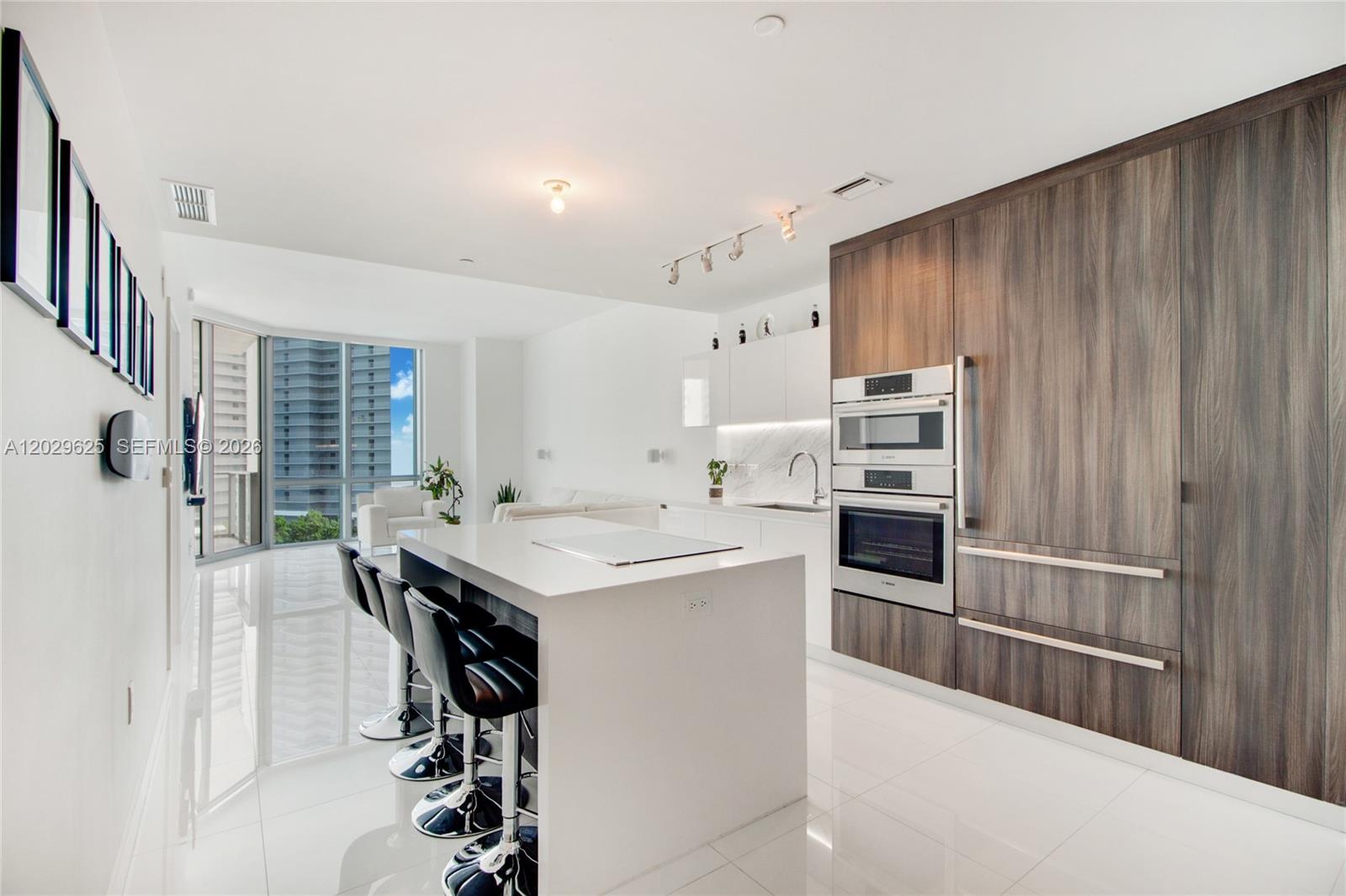 A modern kitchen features a white island, dark wood cabinetry, and stainless steel built-in appliances — 851 NE 1st Ave # 1705, Miami FL 33132, MIAMI, FL