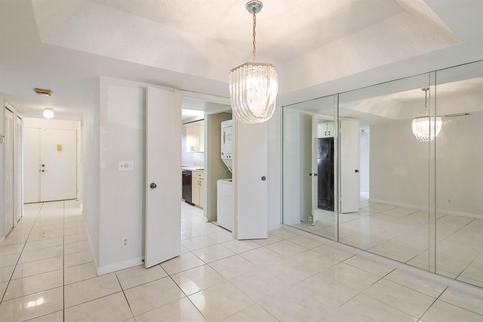 A tiled entryway features a crystal chandelier, mirrored closet doors, and a view into the kitchen — 6850 10th Avenue N # 406, FL 33467, FL