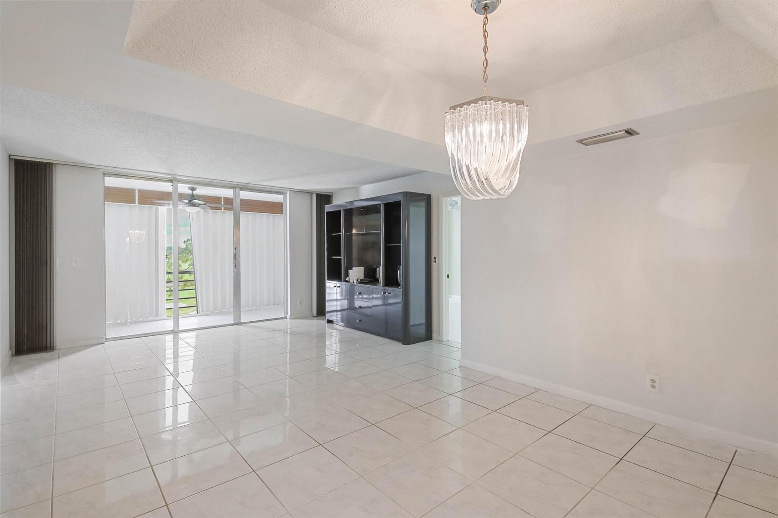 A bright dining area features white tile floors, a crystal chandelier, and sliding glass doors — 6850 10th Avenue N # 406, FL 33467, FL