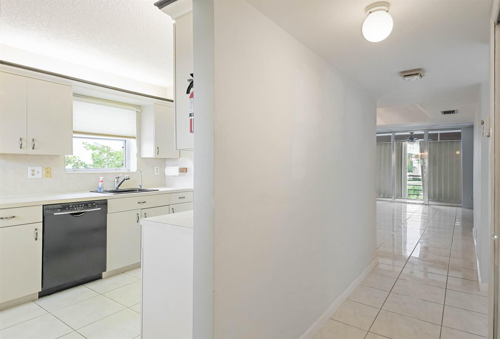 A kitchen with white cabinets and a black dishwasher opens into a tiled hallway — 6850 10th Avenue N # 406, FL 33467, FL