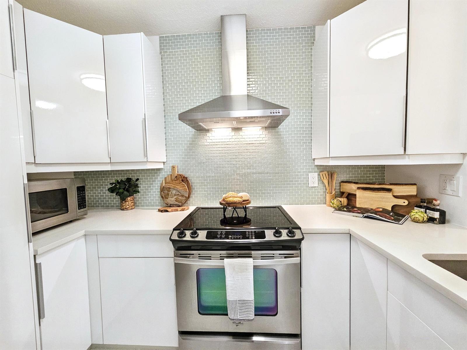 A modern kitchen features white cabinets, a stainless steel stove, and a light green tiled backsplash — 6530 N Ocean Boulevard # 1080, Ocean Ridge FL 33435, OCEAN RIDGE, FL